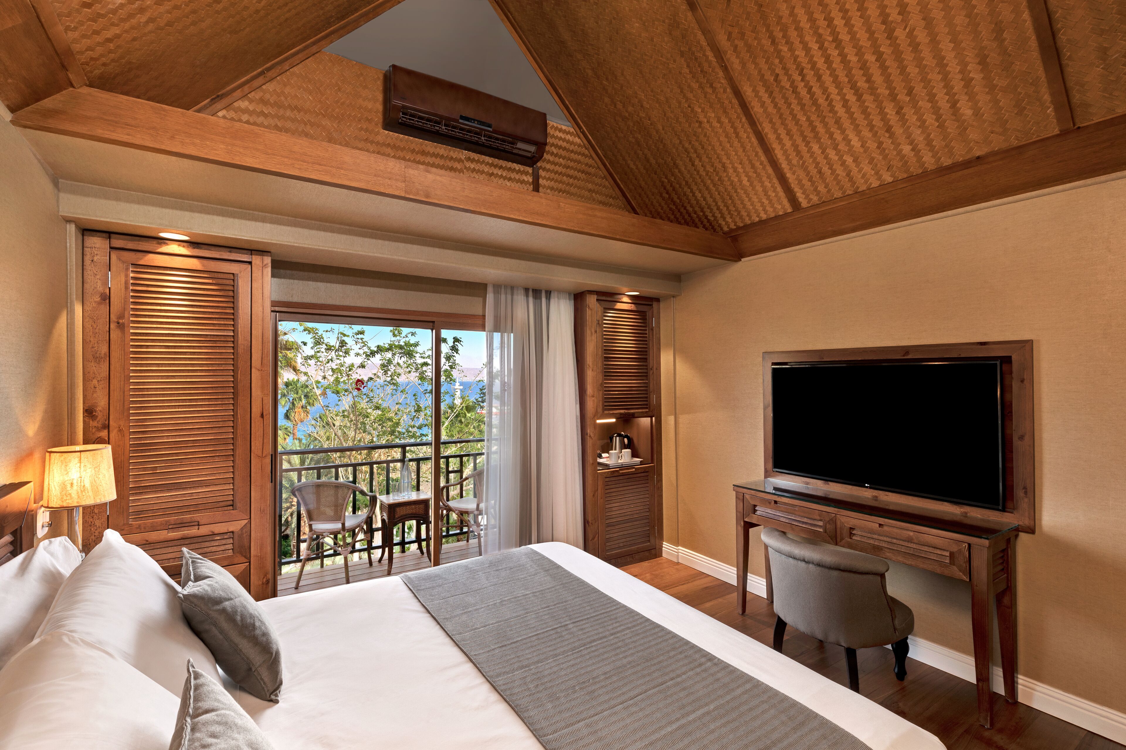 Habitación de hotel con una cama grande, televisión, escritorio y balcón con una silla.