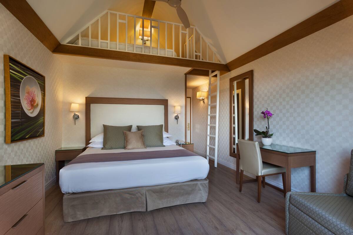 Habitación de hotel con una cama grande, un escritorio, una silla y una escalera que lleva a un nivel superior.