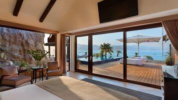 A modern bedroom with a large bed, a TV, and a view of a pool and mountains.
