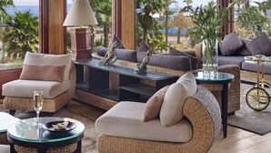 Eine Küstenlounge mit Korbmöbeln, einem Glastisch und Blick auf das Meer.