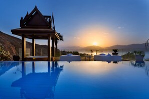 A serene infinity pool with a wooden gazebo and lounge chairs, overlooking a sunset over mountains. - Orchid Eilat - All Inclusive Extra (Eilat)