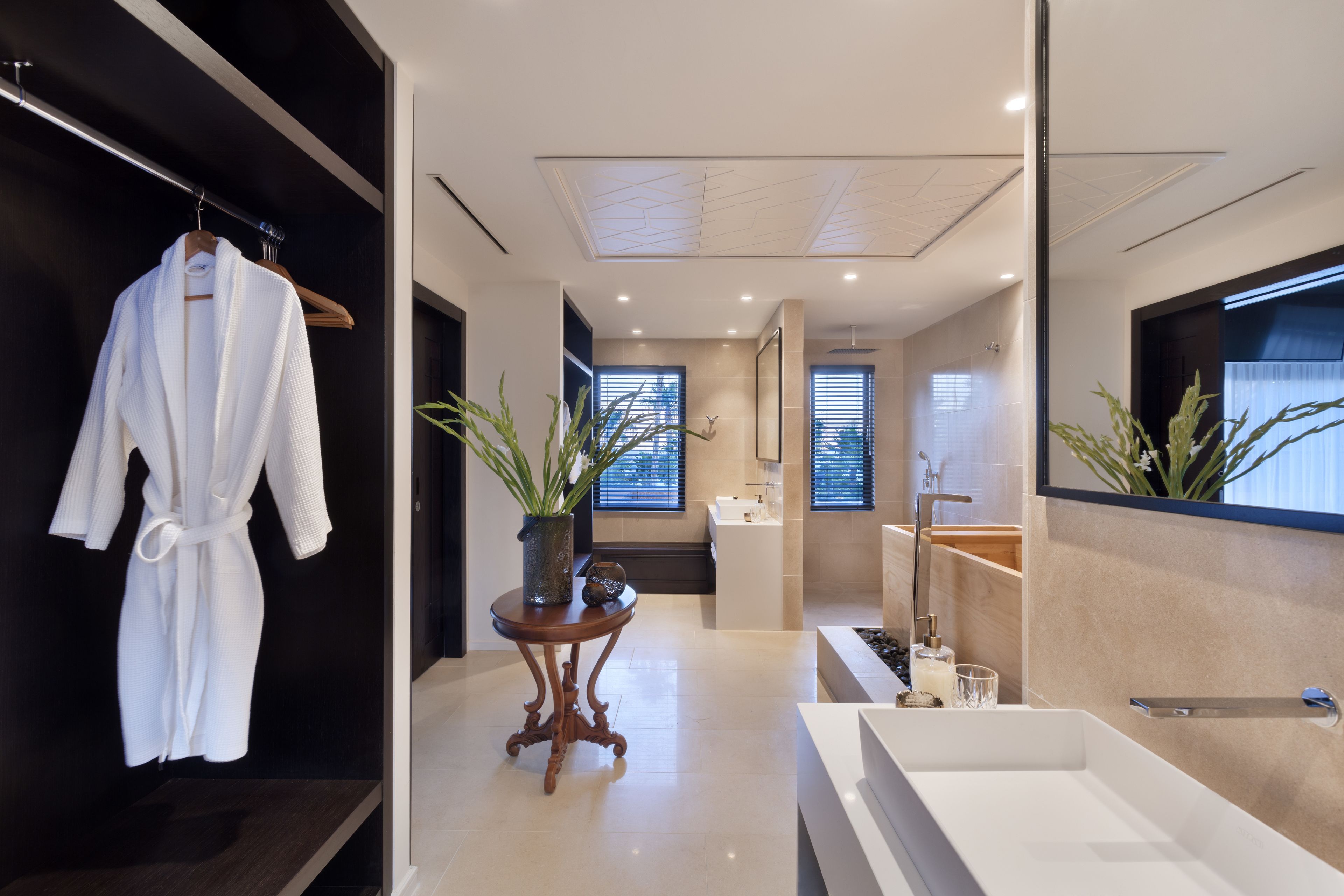 Un baño moderno con una bañera grande, una bata colgada en un perchero y una planta en maceta sobre una mesita.