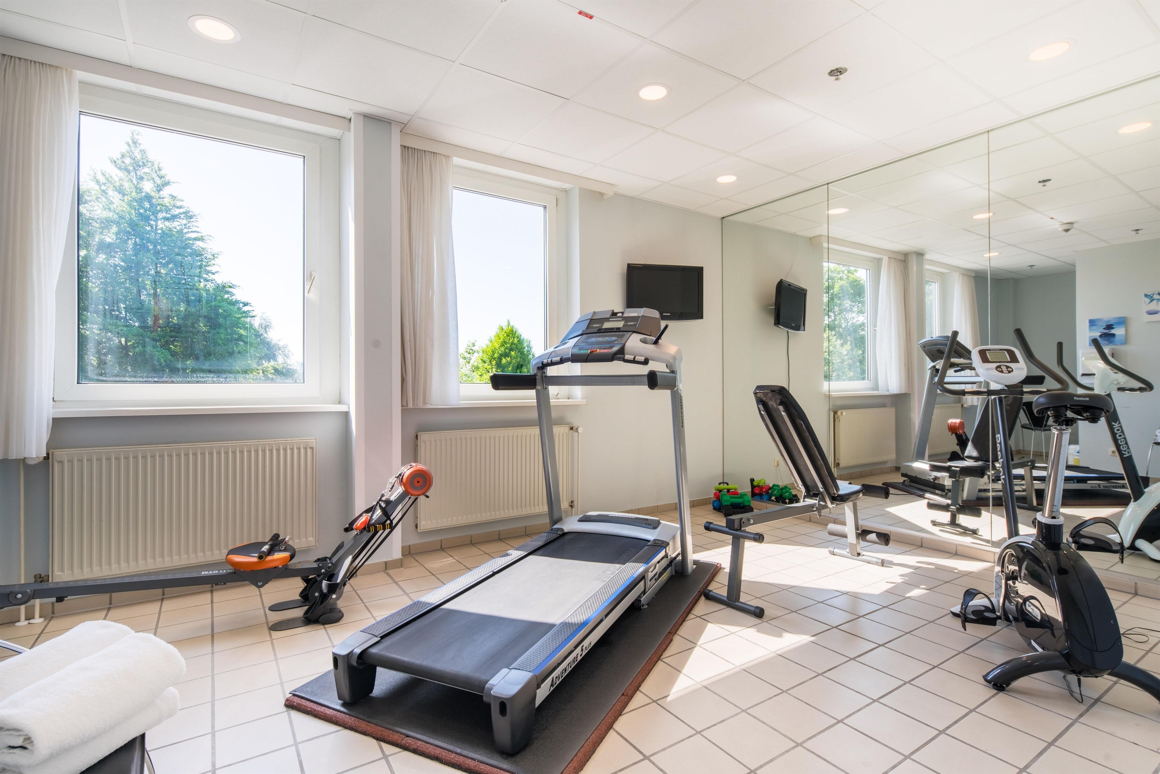 Ein Fitnessstudio mit Trainingsgeräten, großen Fenstern und Blick auf Bäume.