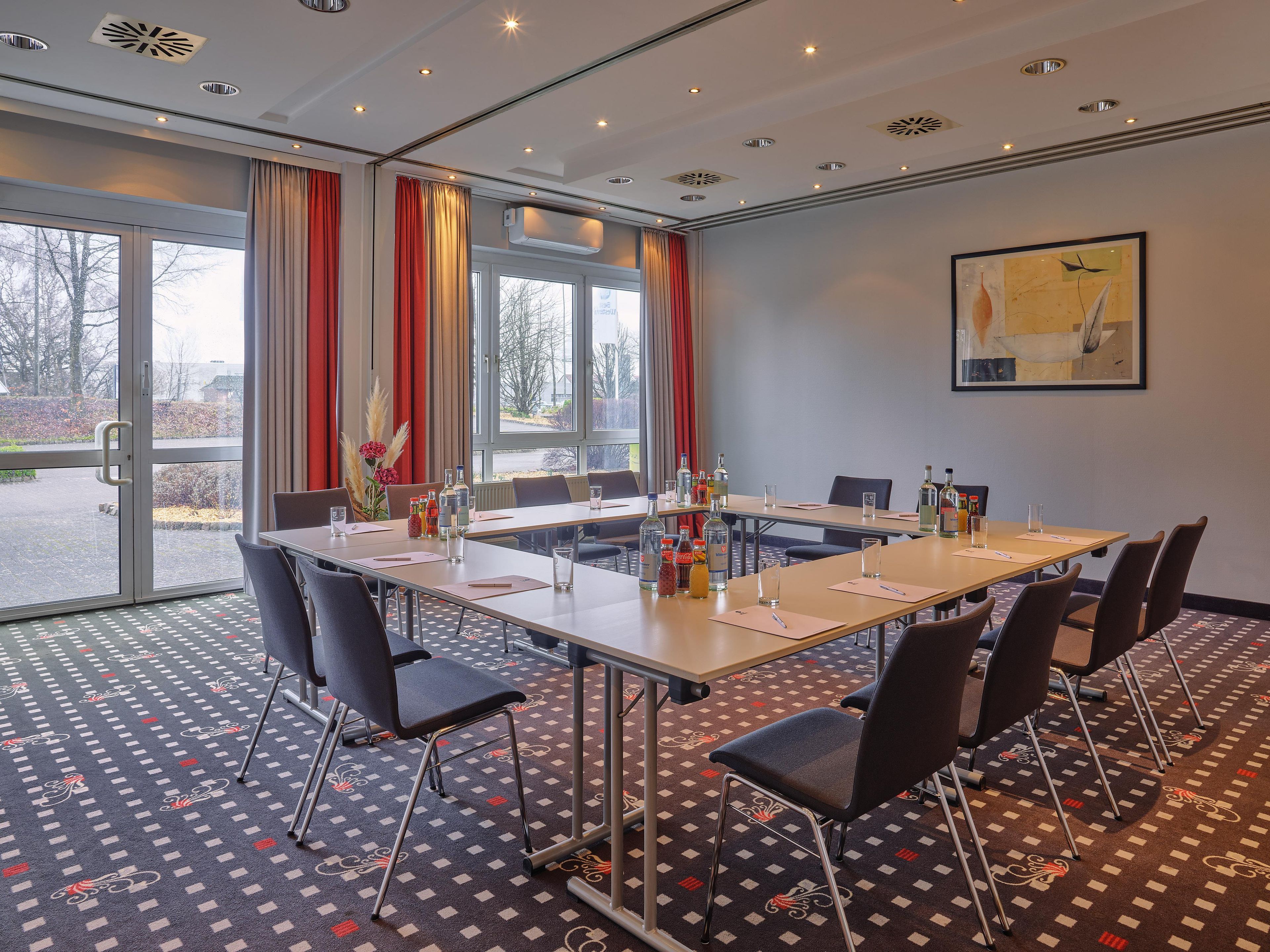 Ein Konferenzraum mit einem langen Tisch, Stühlen und einem großen Fenster mit Vorhängen.