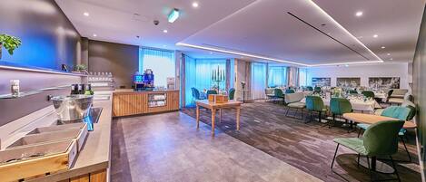 A modern hotel lobby with a reception desk, seating area, and a large window with curtains.