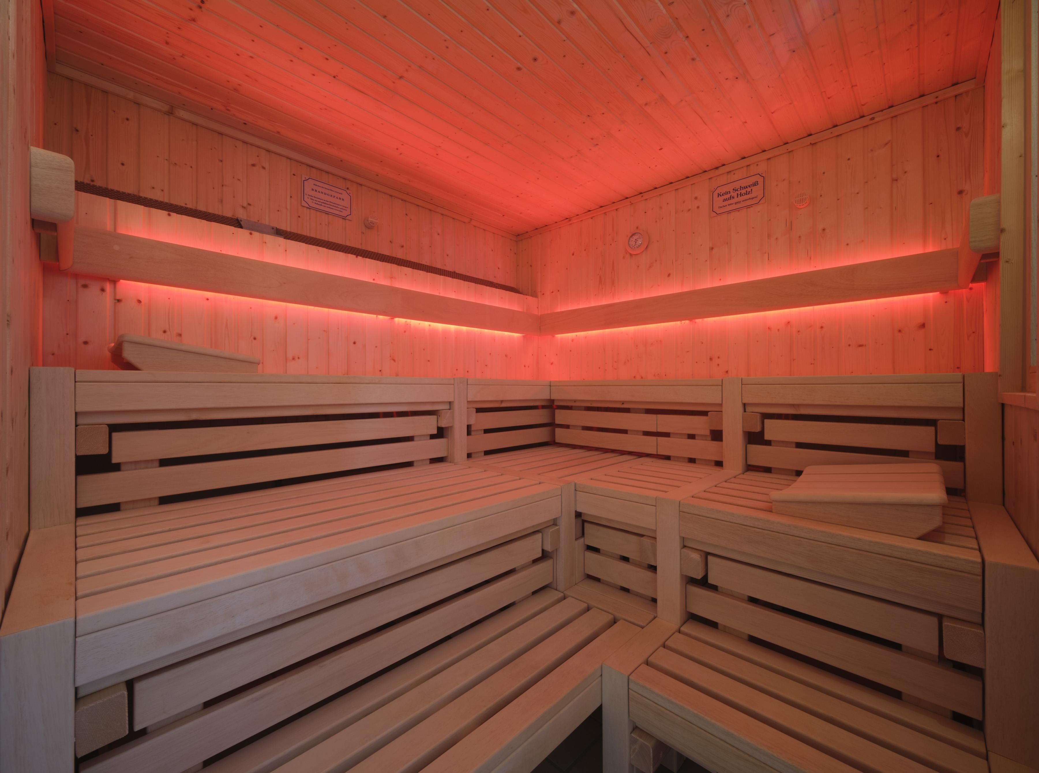 Un sauna avec des bancs en bois et une ambiance éclairée de lumière rouge.