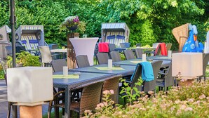 An outdoor dining area with wicker furniture and a large umbrella. - Best Western Hotel Prisma (Neumuenster)