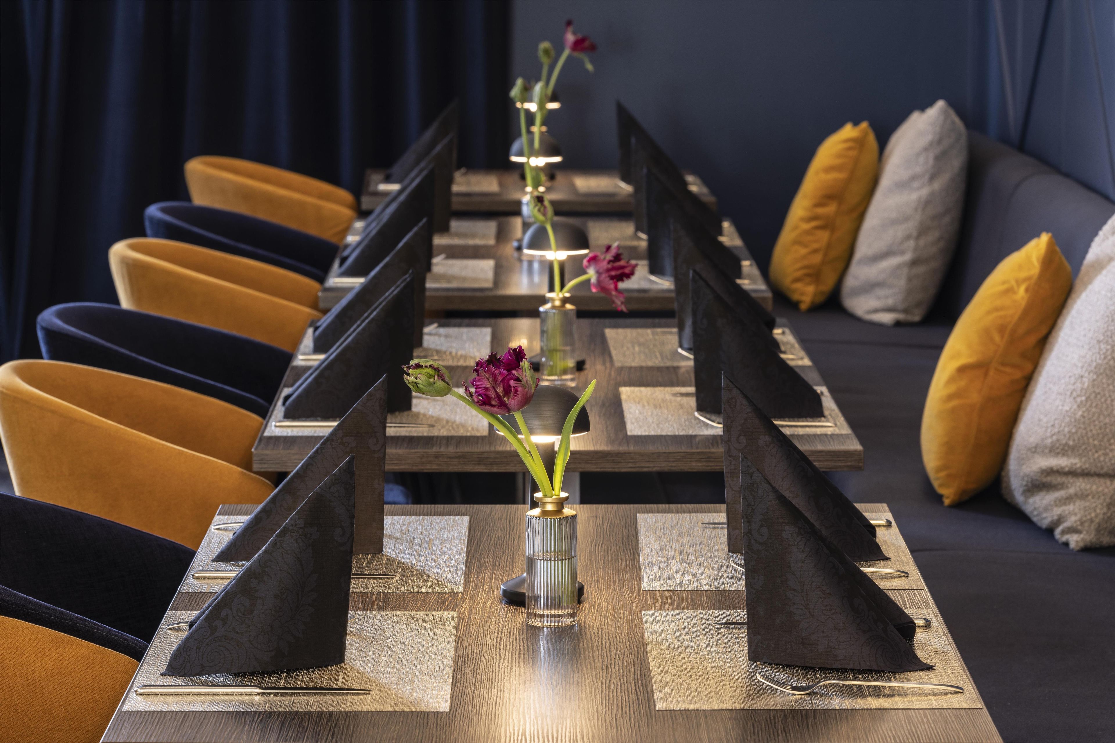 A long table with a vase of flowers, black napkins, and a row of chairs.