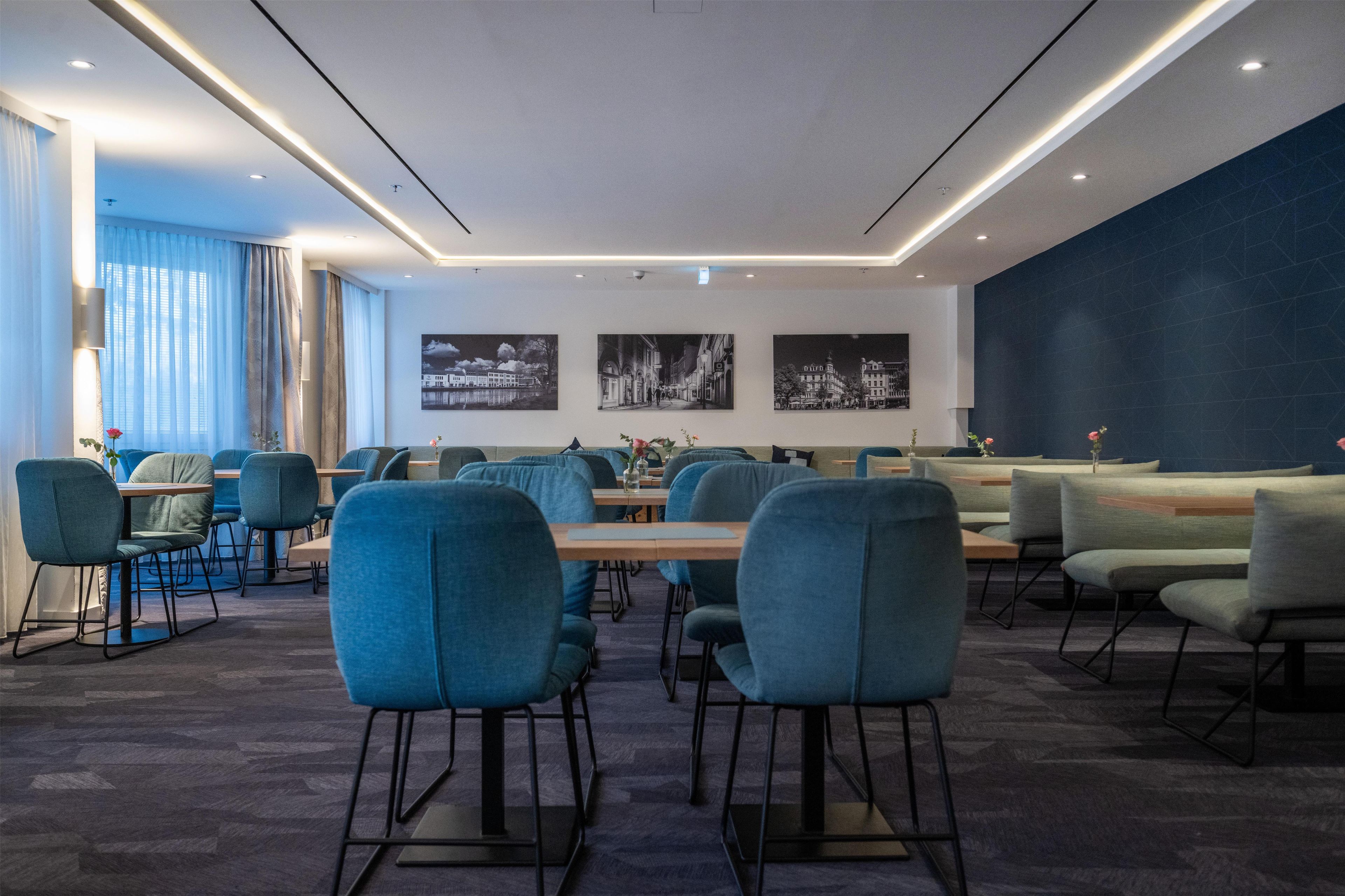 Una sala conferenze moderna con sedie blu, un lungo tavolo e opere d'arte raffiguranti un panorama urbano alle pareti.