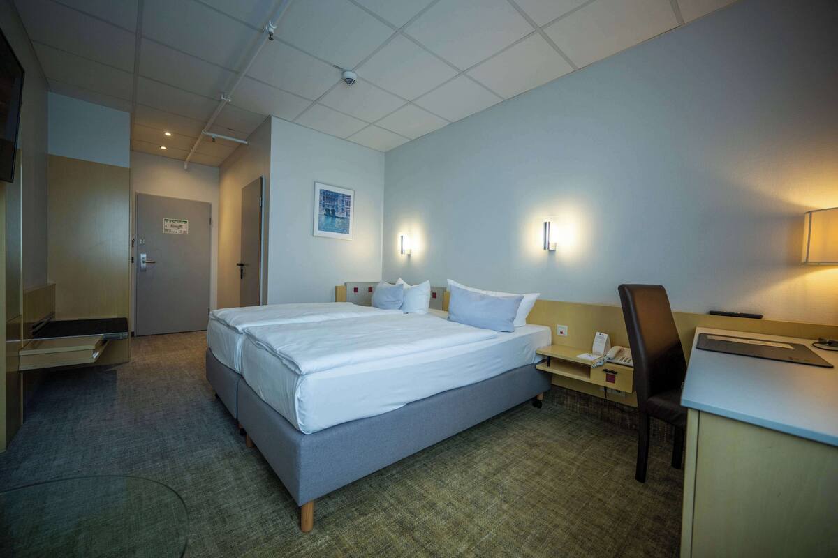 A hotel room with a large bed, bedside tables, a desk, and a chair.