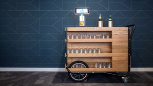 A wooden cart with shelves containing glasses and bottles, against a dark blue tiled wall. - Best Western Hotel Prisma (Neumuenster)