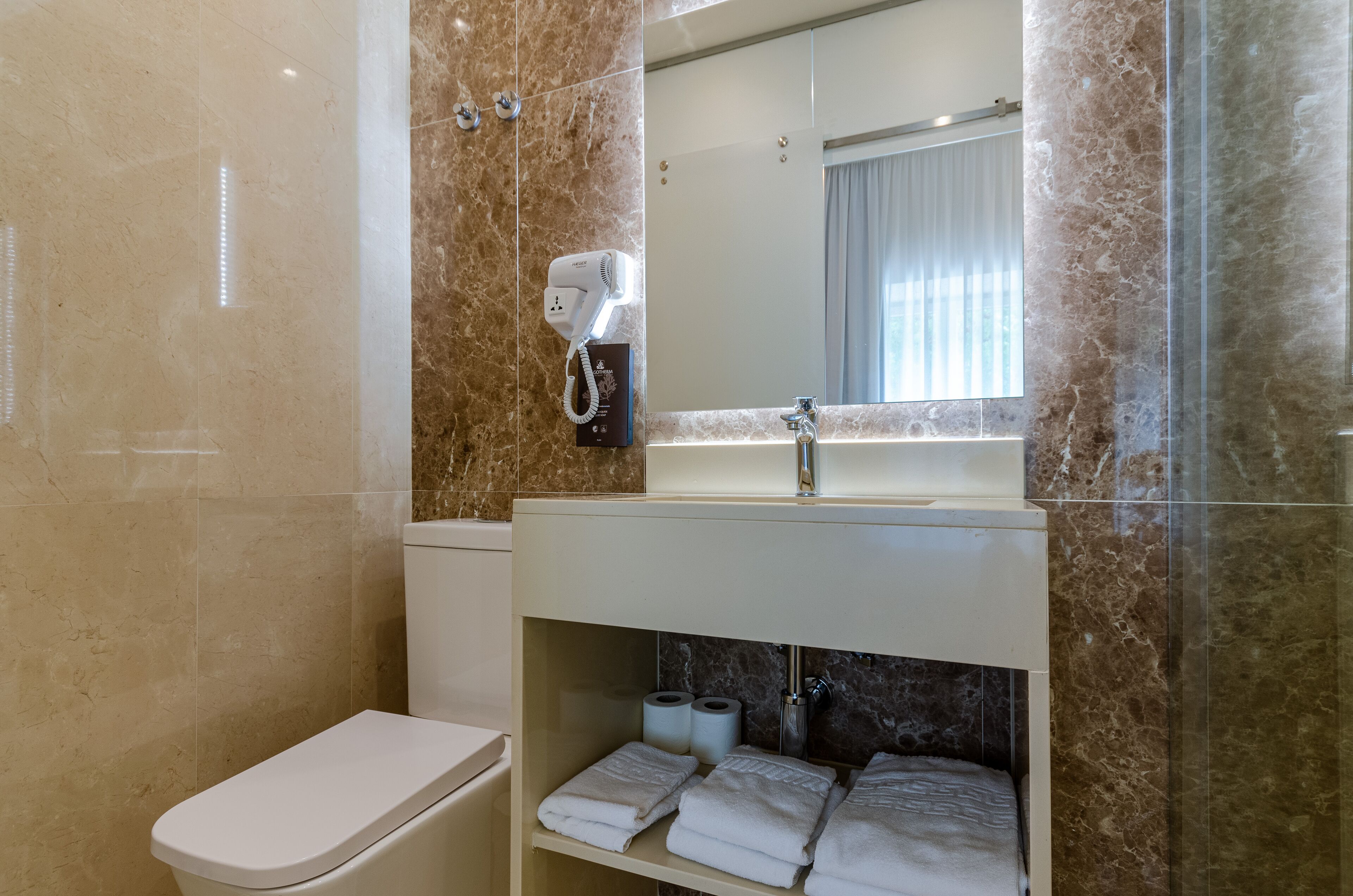 A bathroom with a toilet, a sink, a mirror, a hairdryer, and towels.
