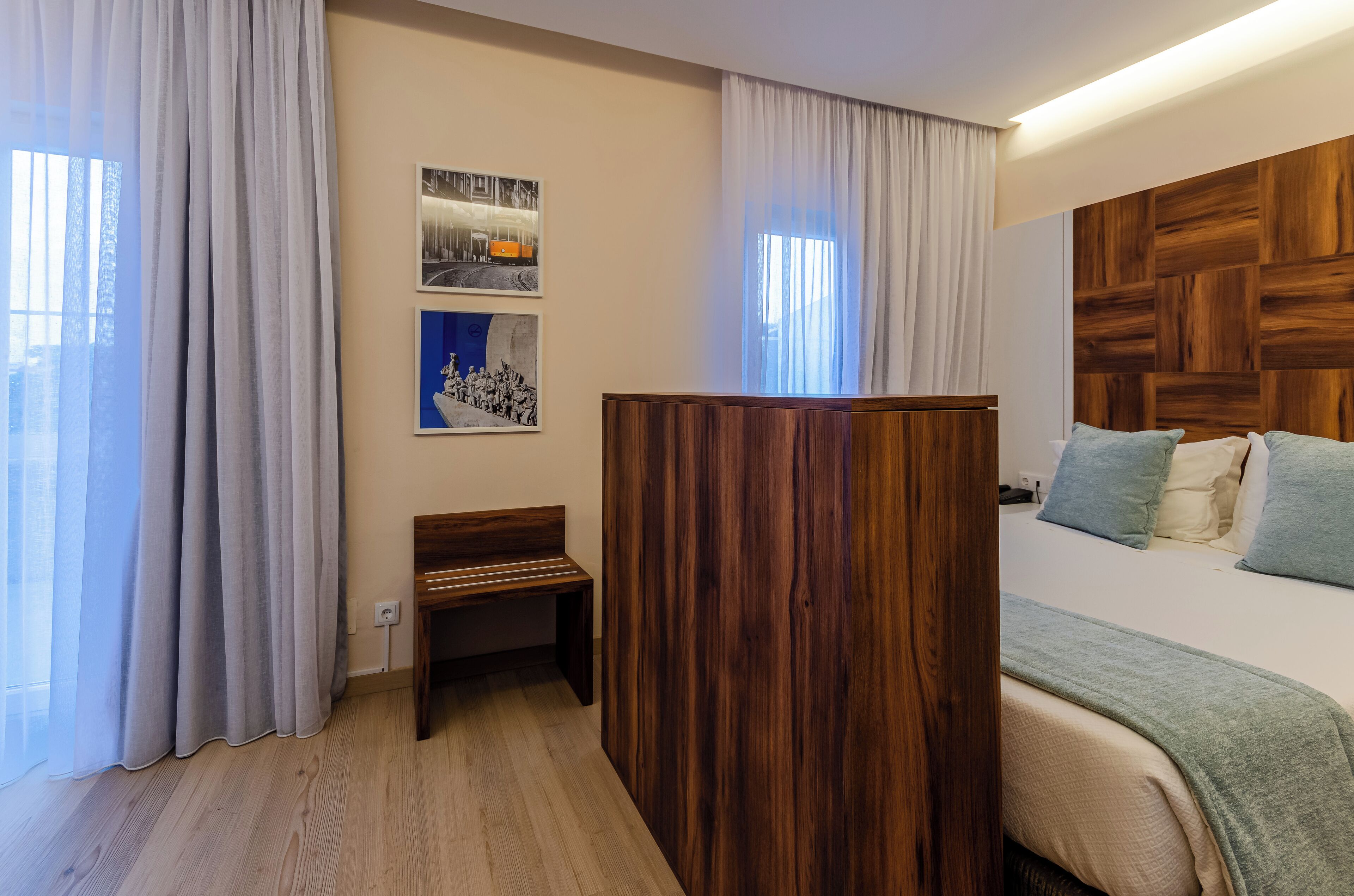 Une chambre d’hôtel moderne avec une tête de lit en bois, un lit agrémenté d’oreillers bleus et blancs, un banc et des œuvres d’art accrochées au mur.