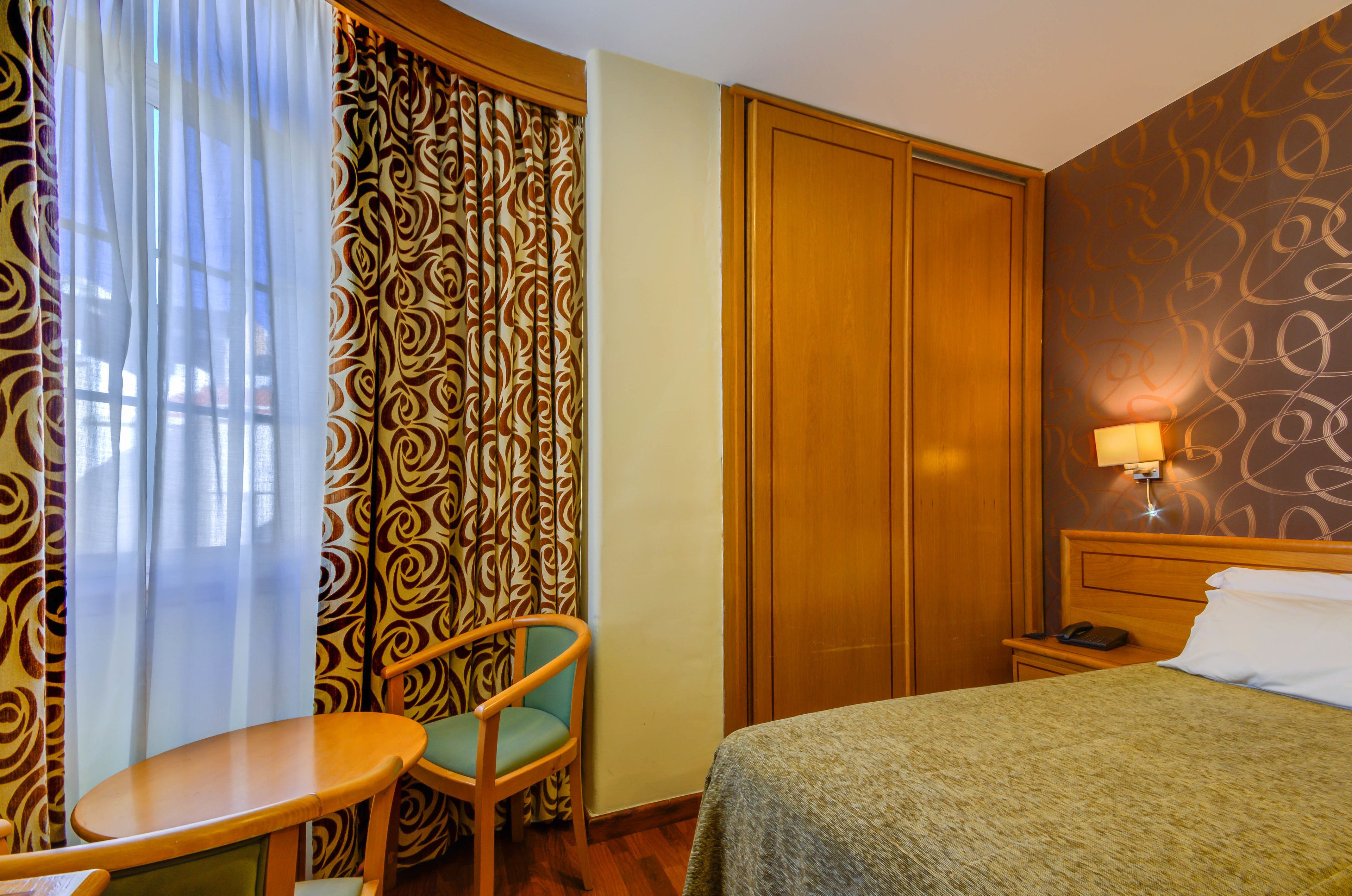 Una camera d'albergo con un letto, una sedia, un tavolo, un armadio e una lampada.