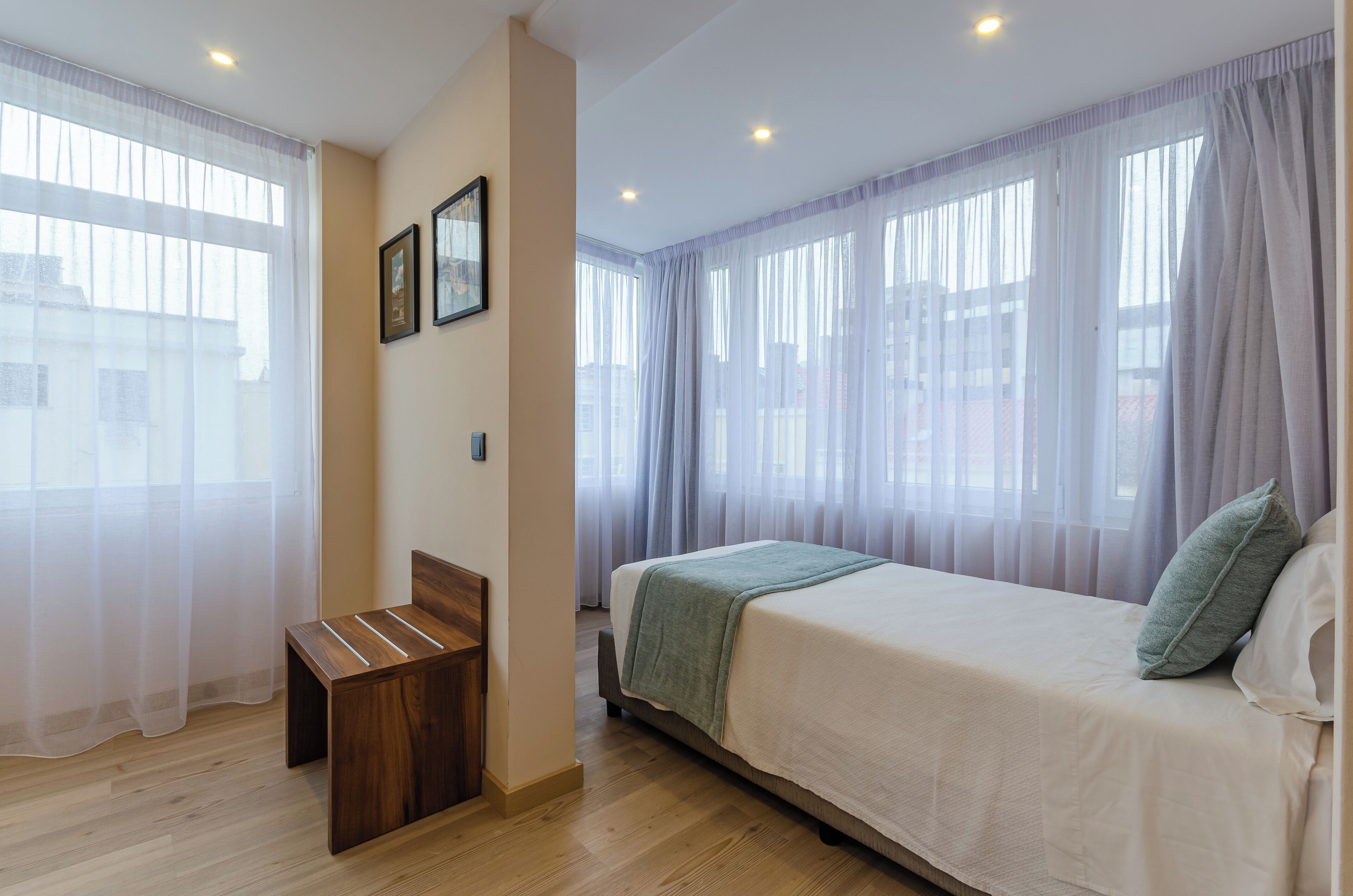 A bedroom with a bed, a wooden bench, and sheer curtains.