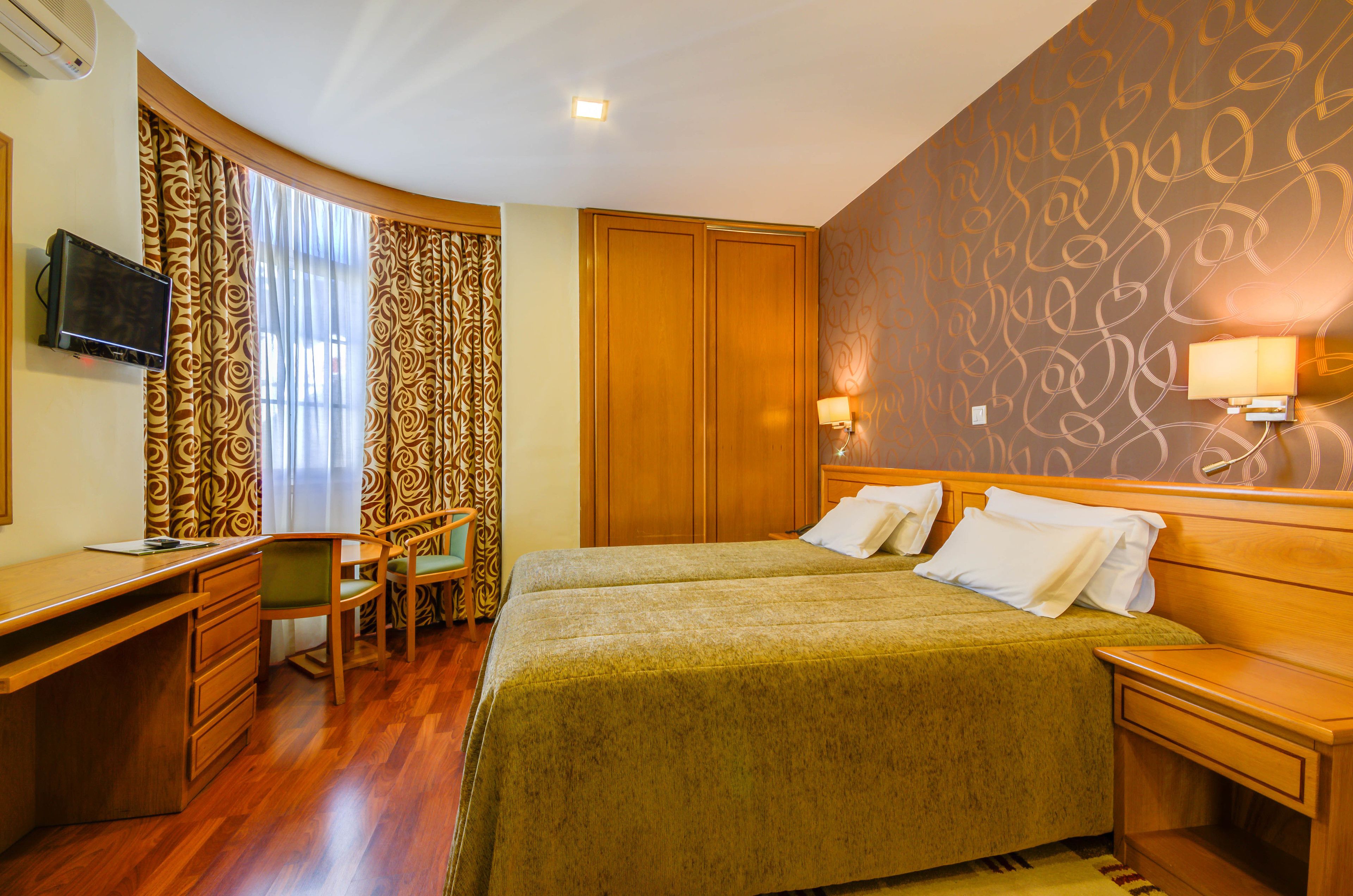 Une chambre d’hôtel équipée d’un lit, d’un bureau, d’une chaise et d’un téléviseur fixé au mur.