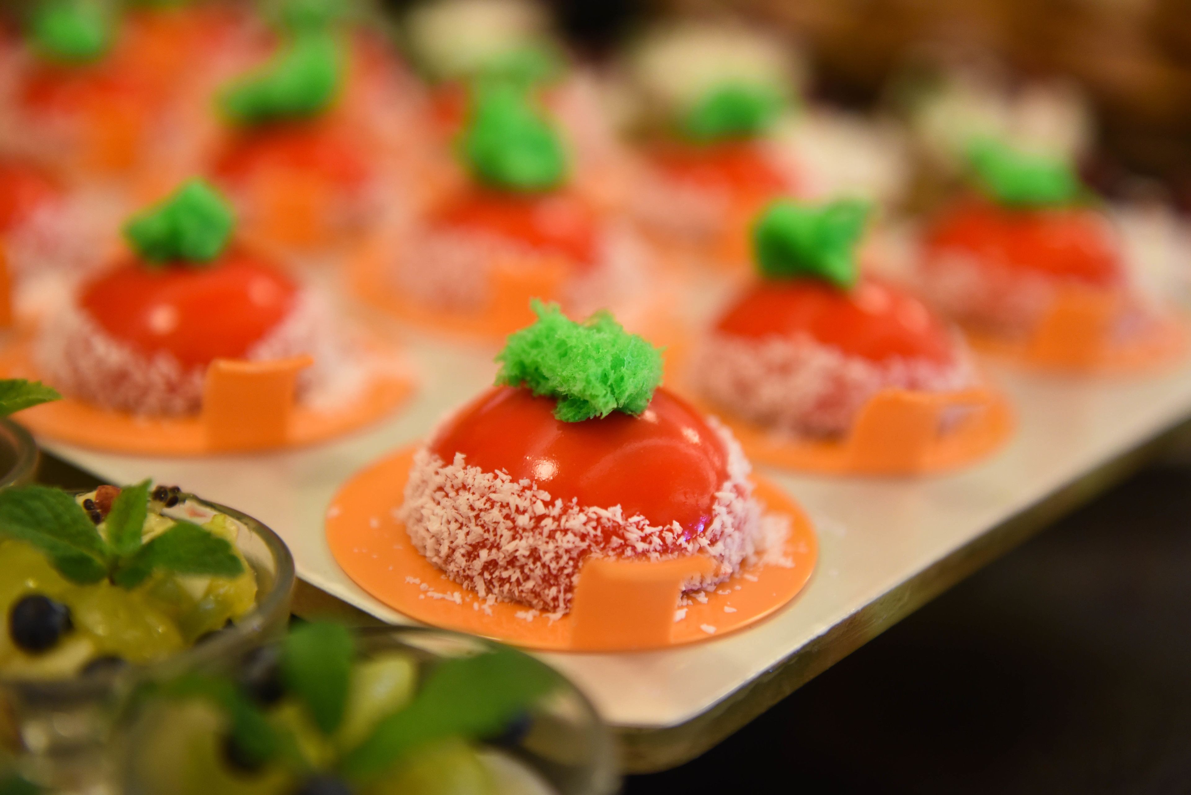 Una bandeja de postres con bolitas rojas coronadas con adornos verdes, rodeada de platos naranjas.