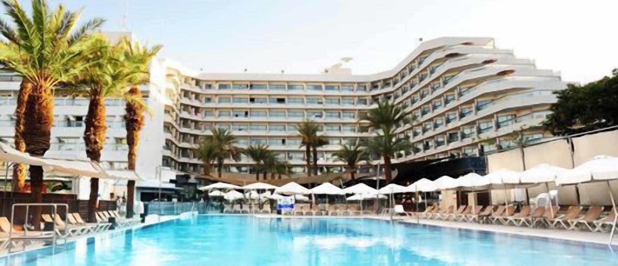 Un hotel con piscina, varios balcones y palmeras.