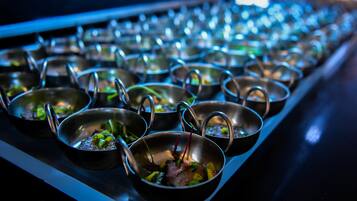 A row of metal bowls with handles, each containing food, arranged on a tray.