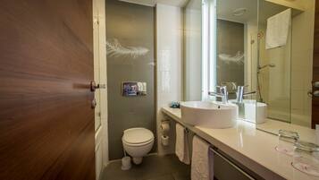 Un baño moderno con puerta de madera, inodoro, lavamanos con espejo y zona de ducha.