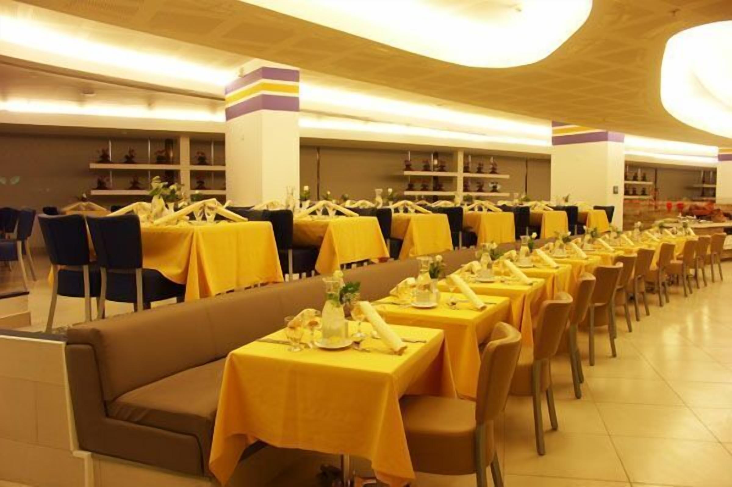 A restaurant with multiple tables and chairs, each set with yellow tablecloths and neatly arranged table settings.