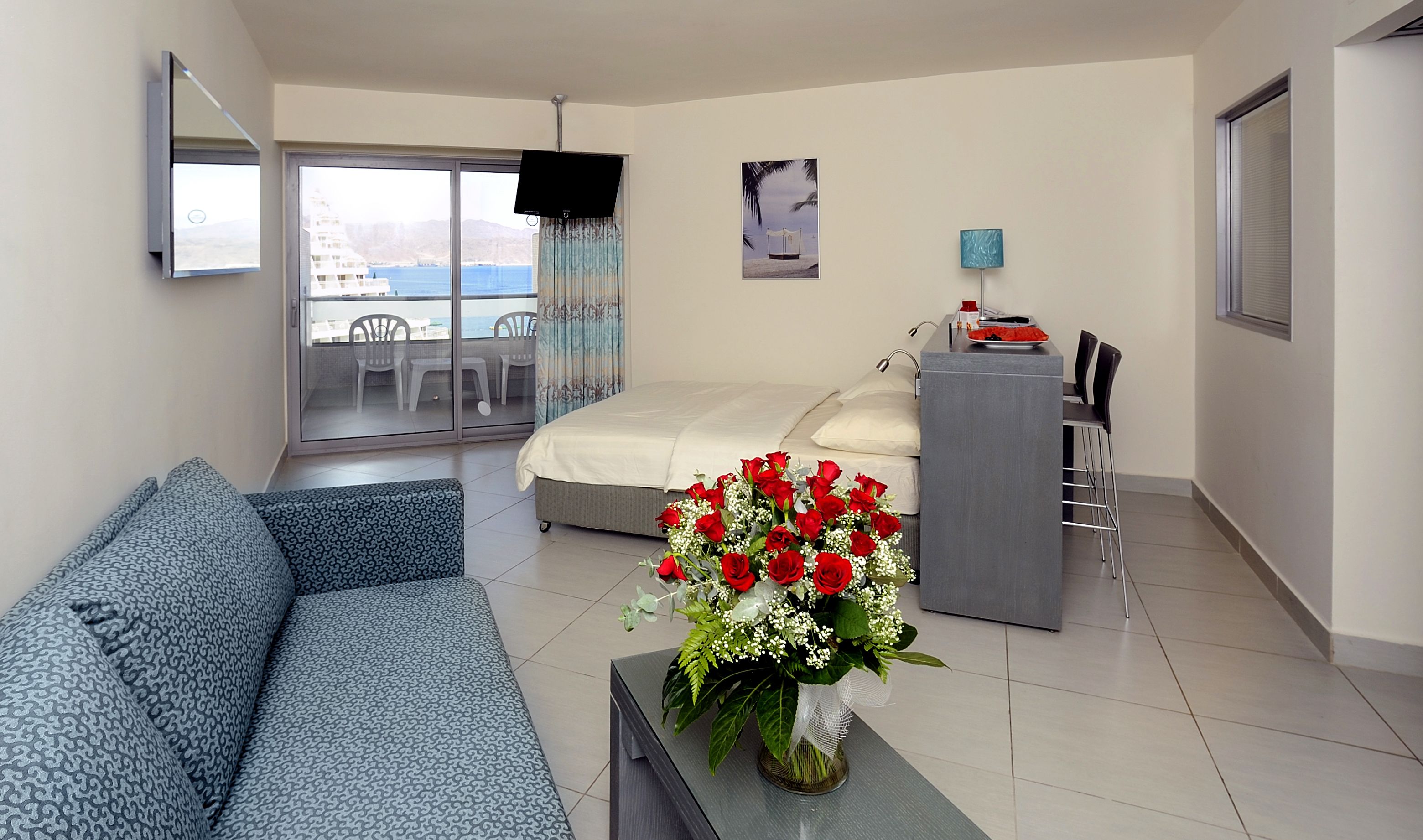 Ein modernes Hotelzimmer mit Balkon, einem Bett, einem Schreibtisch und einer Couch.