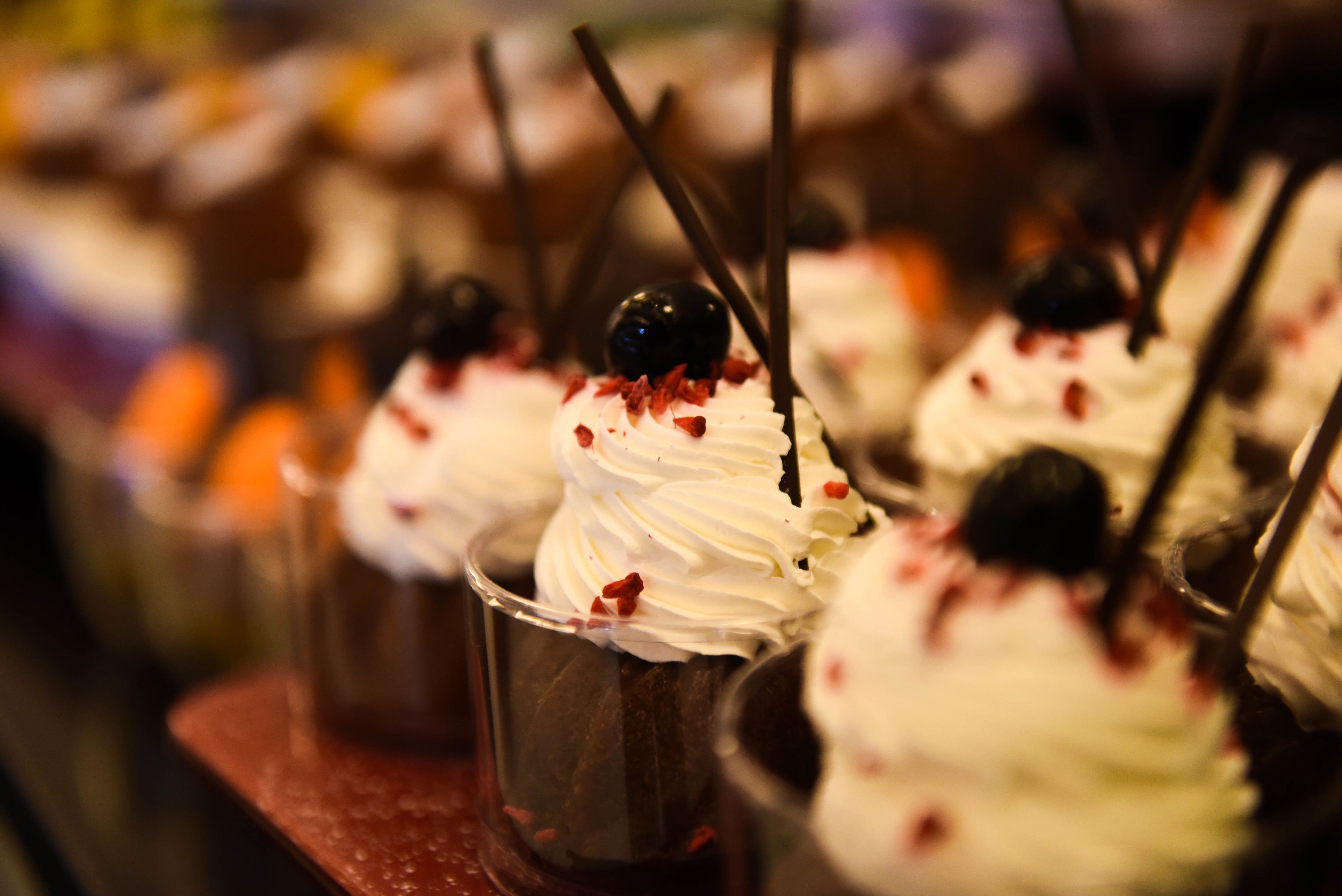A dessert display with various sweets topped with whipped cream and cherries.