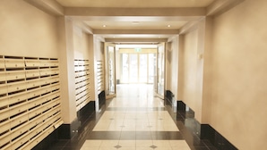 A hotel corridor with a tiled floor, a row of storage lockers on one side, and a door at the end. - Arrow on Spencer (Melbourne)