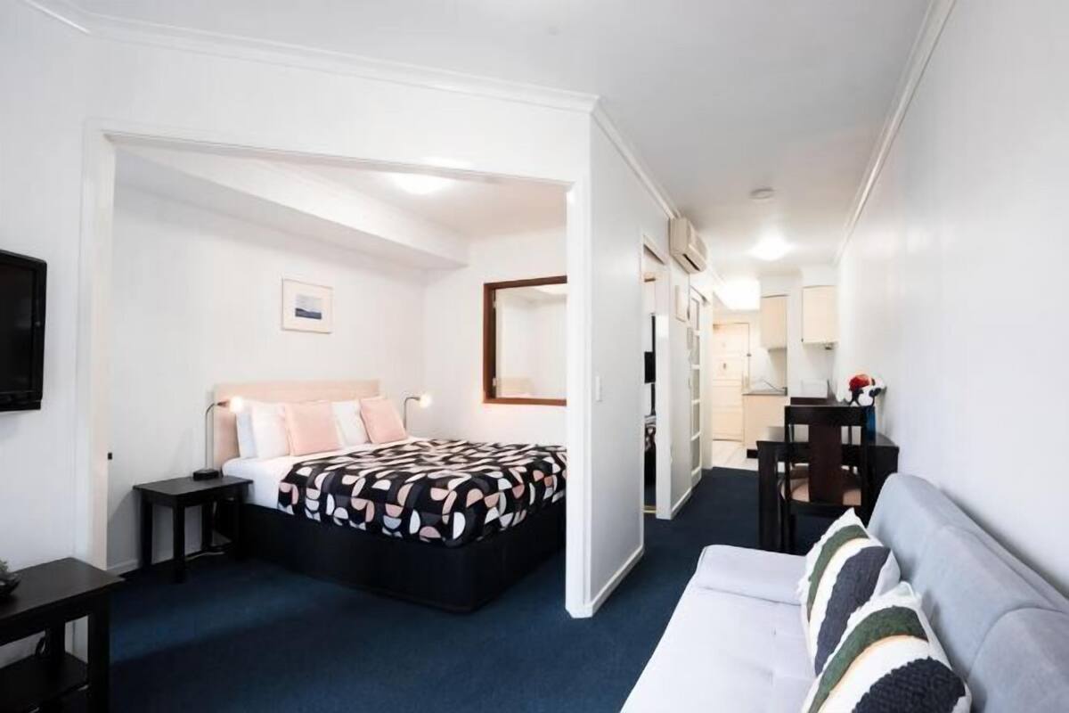Quarto de hotel com uma cama, uma escrivaninha, uma cadeira, um sofá e uma televisão.