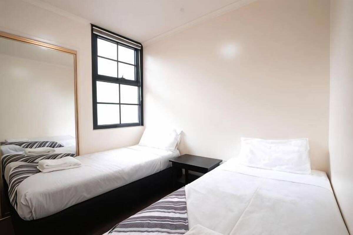 Quarto com duas camas, uma janela e um espelho.