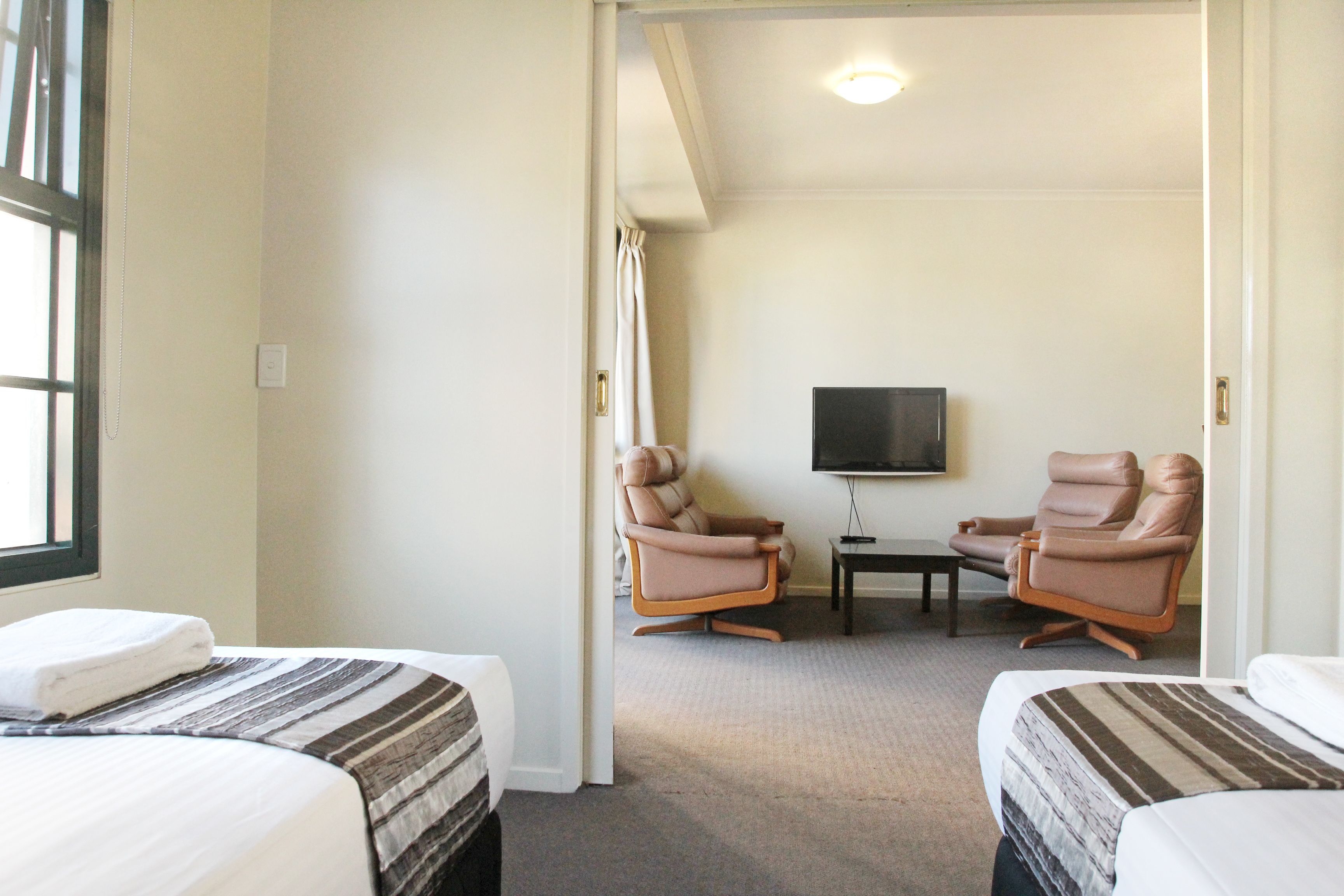 A hotel room with two beds, a television, and two leather chairs.