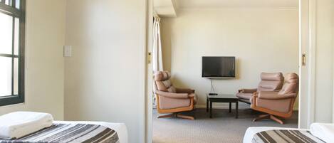 A hotel room with two beds, a television, and two leather chairs.