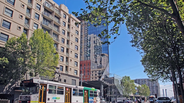 A tram on a city street with buildings and trees. - Arrow on Spencer (Melbourne)