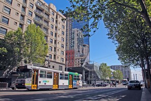 A tram on a city street with buildings and trees. - Arrow on Spencer (Melbourne)