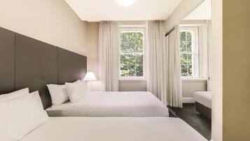 Habitación de hotel con dos camas, un ventanal con cortinas, una lámpara de techo y un cabecero oscuro.