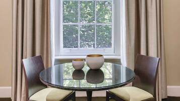 A room with a round glass table, two chairs, and a window with curtains.