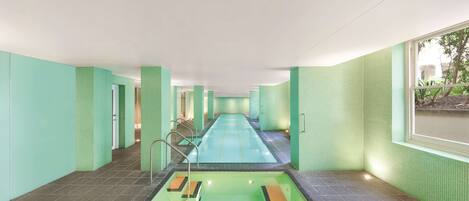 Una piscina con suelo de baldosas, rodeada de paredes con un diseño de baldosas verdes.