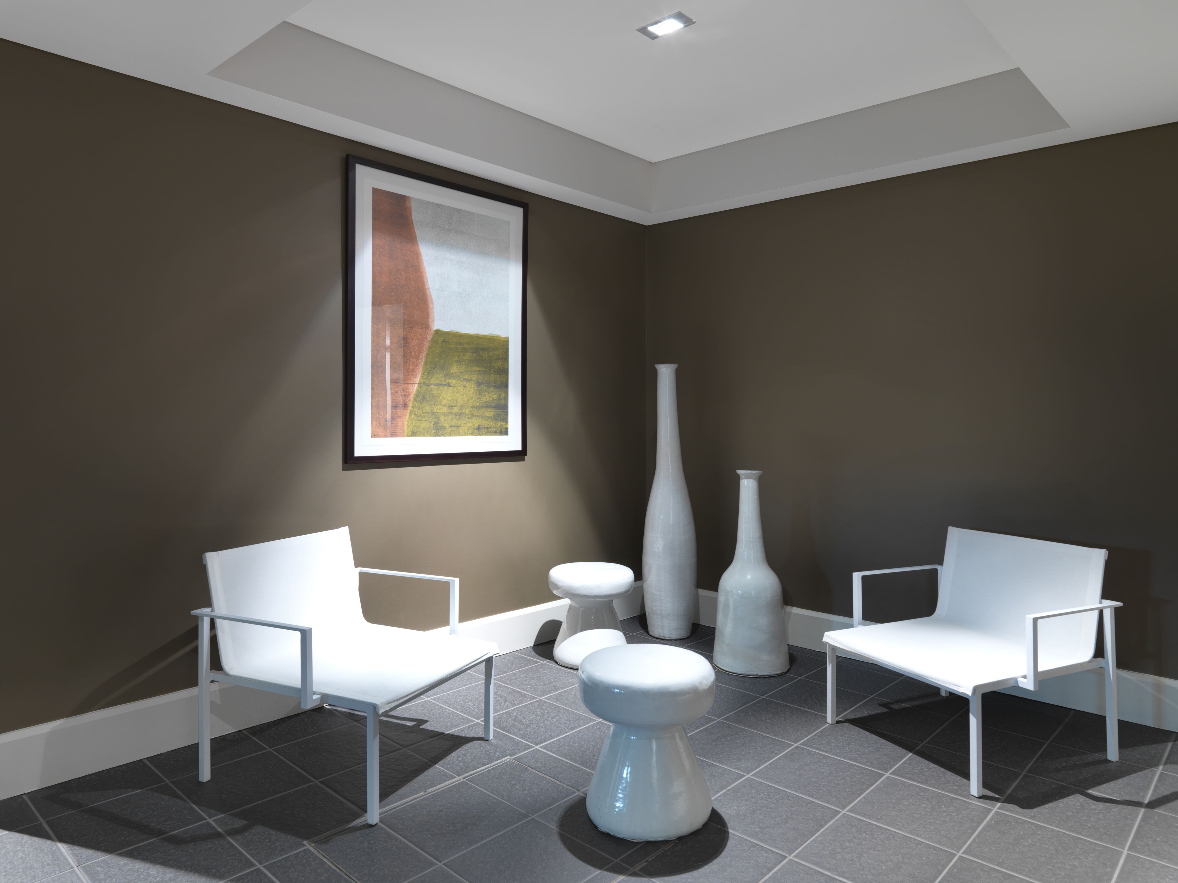 A modern waiting room with two white chairs, a small round table, and a tall vase.