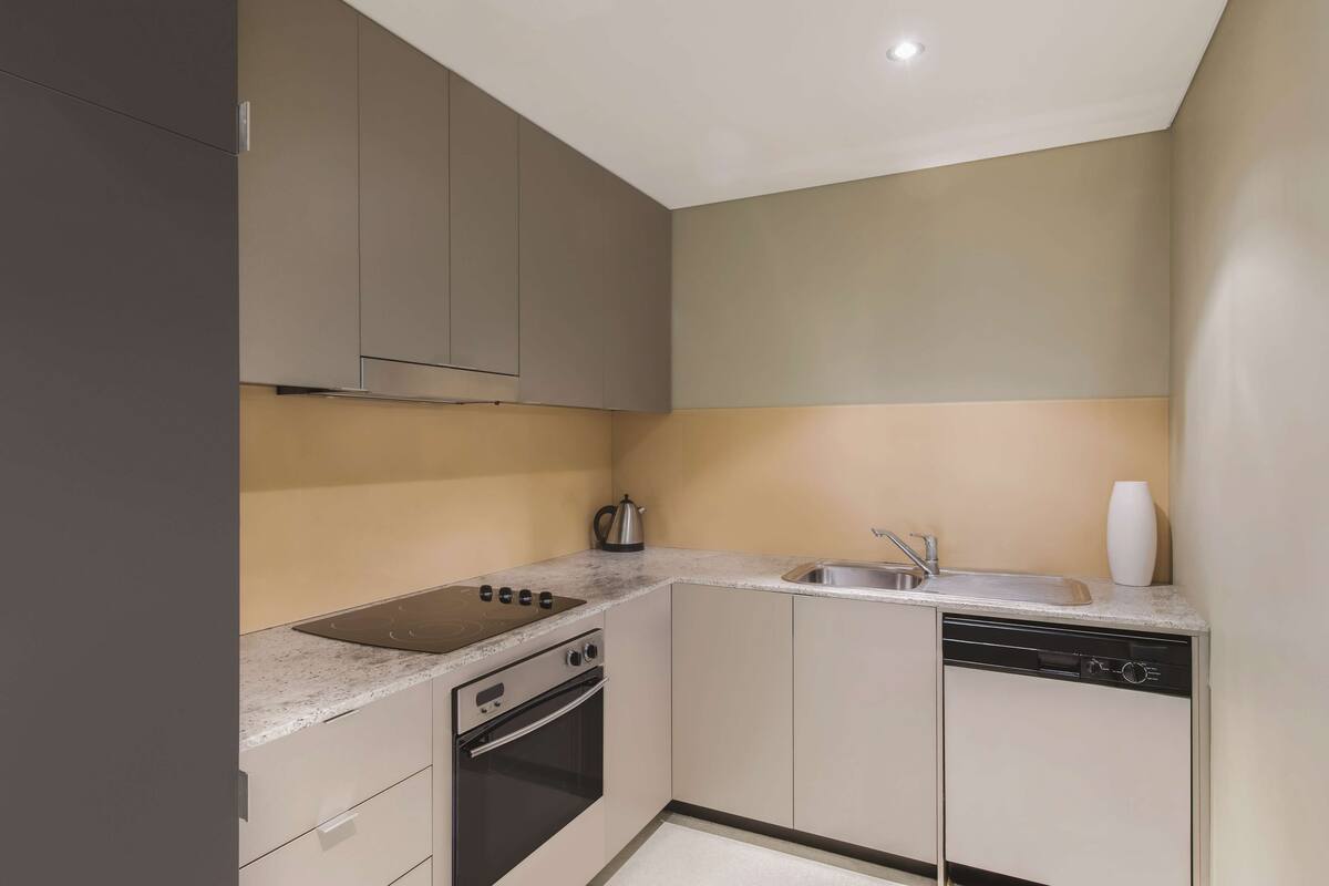 A compact kitchen with a built-in stove, oven, and dishwasher, featuring neutral color tones and modern cabinetry.
