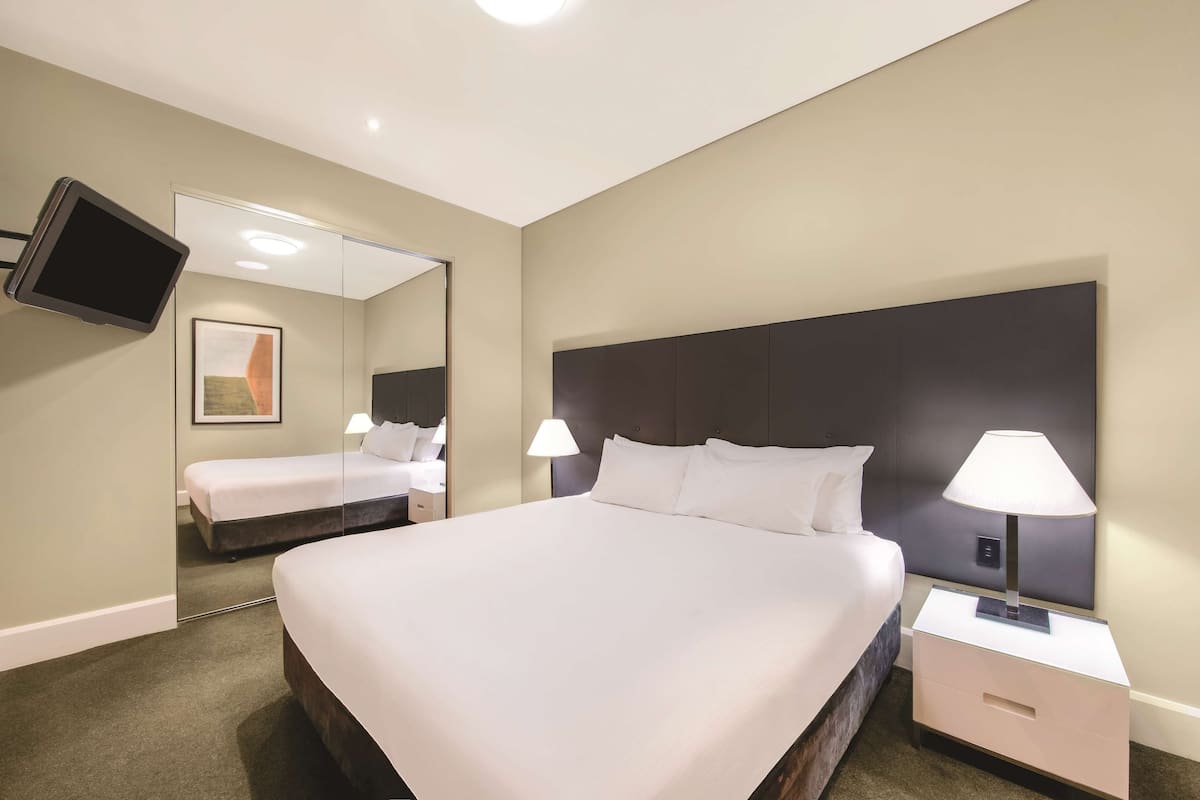 A hotel room with a large bed, two bedside tables with lamps, a flat-screen TV mounted on the wall, and a mirror.
