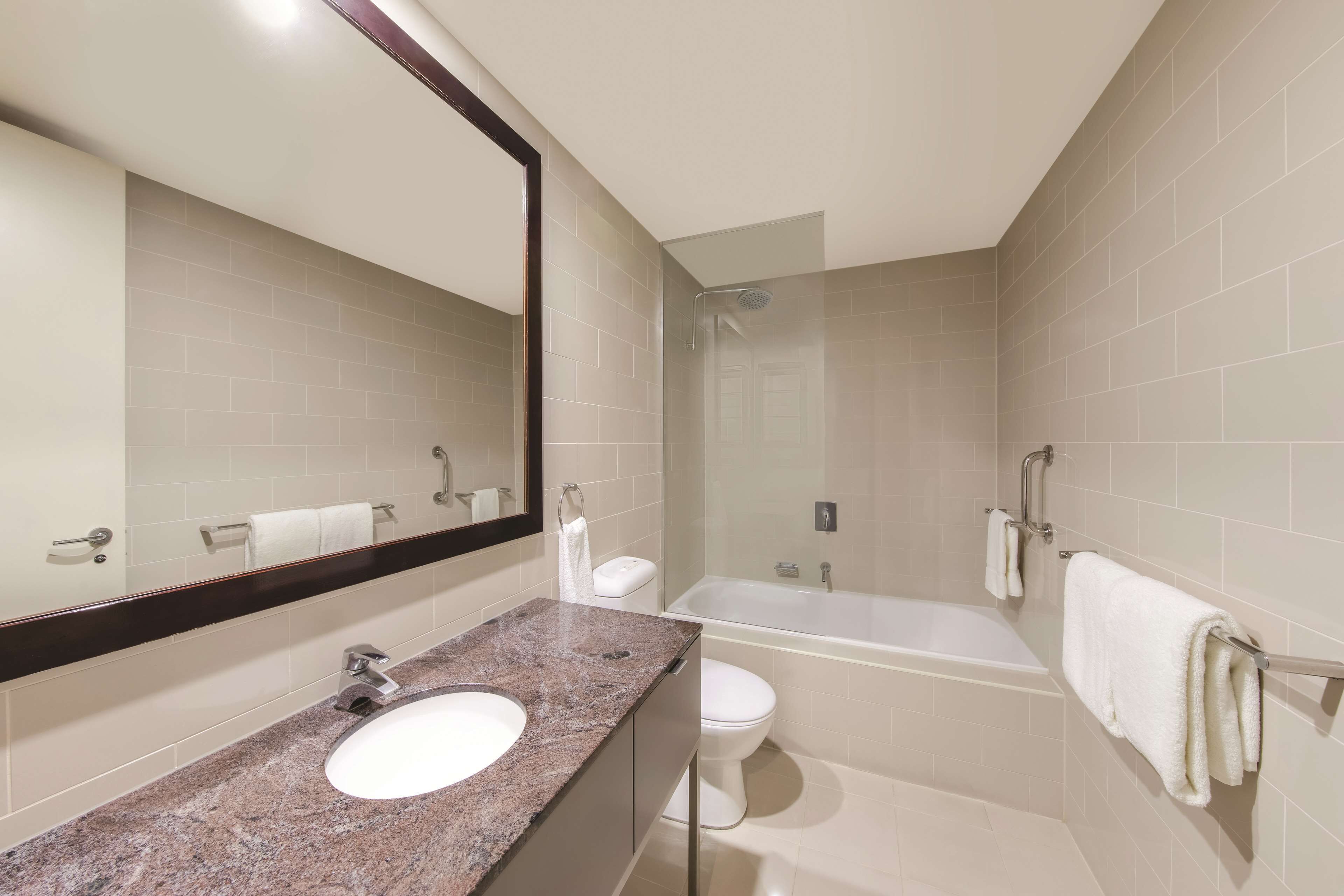 Une salle de bain moderne avec un lavabo surmonté d’un plan en granit, des toilettes blanches, une baignoire et un grand miroir.