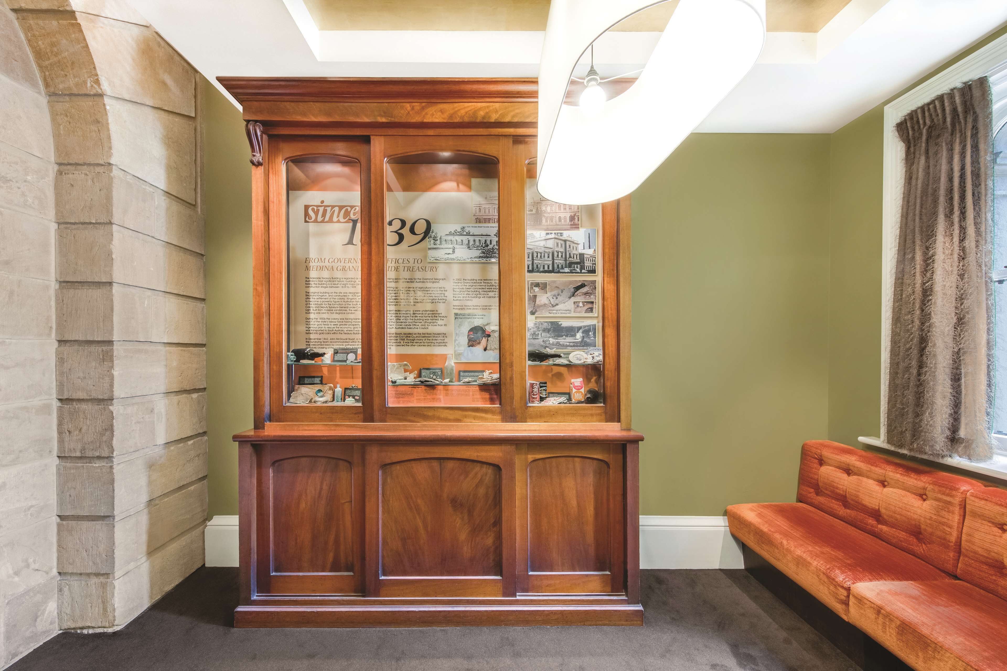 A wooden display case with numbered glass panels, a red sofa, and a window with curtains.