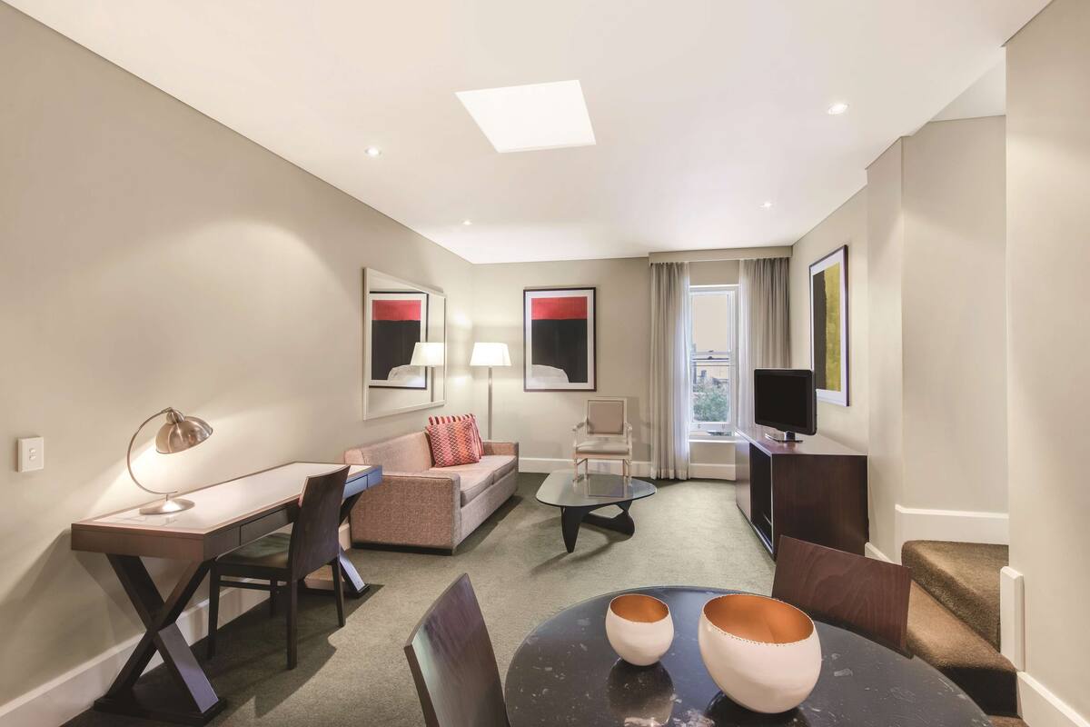 A modern hotel room with a desk, sofa, and TV.