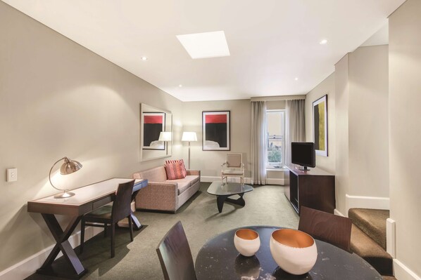 A modern hotel room with a desk, sofa, and TV.