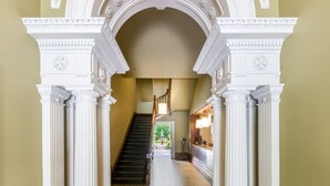 A hallway with white columns, a patterned floor, and a staircase in the background.