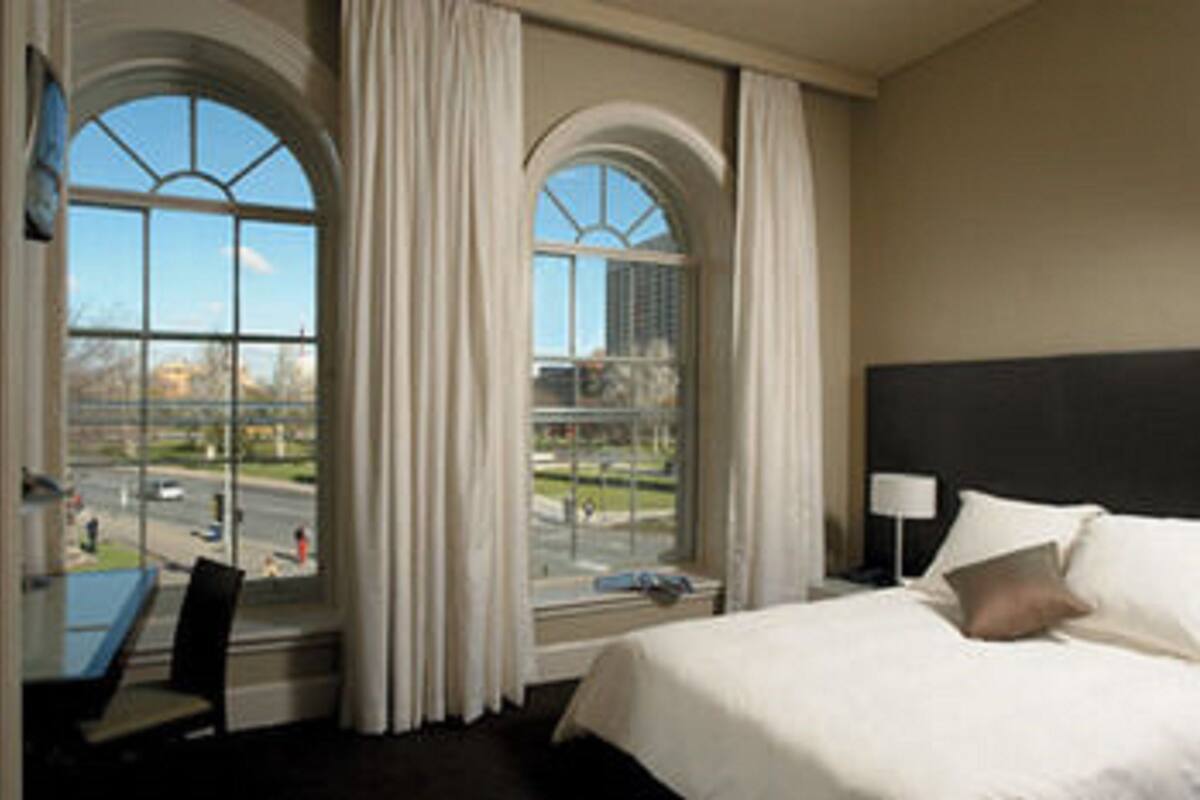 A hotel room with a large bed, a desk with a chair, and two windows with curtains.