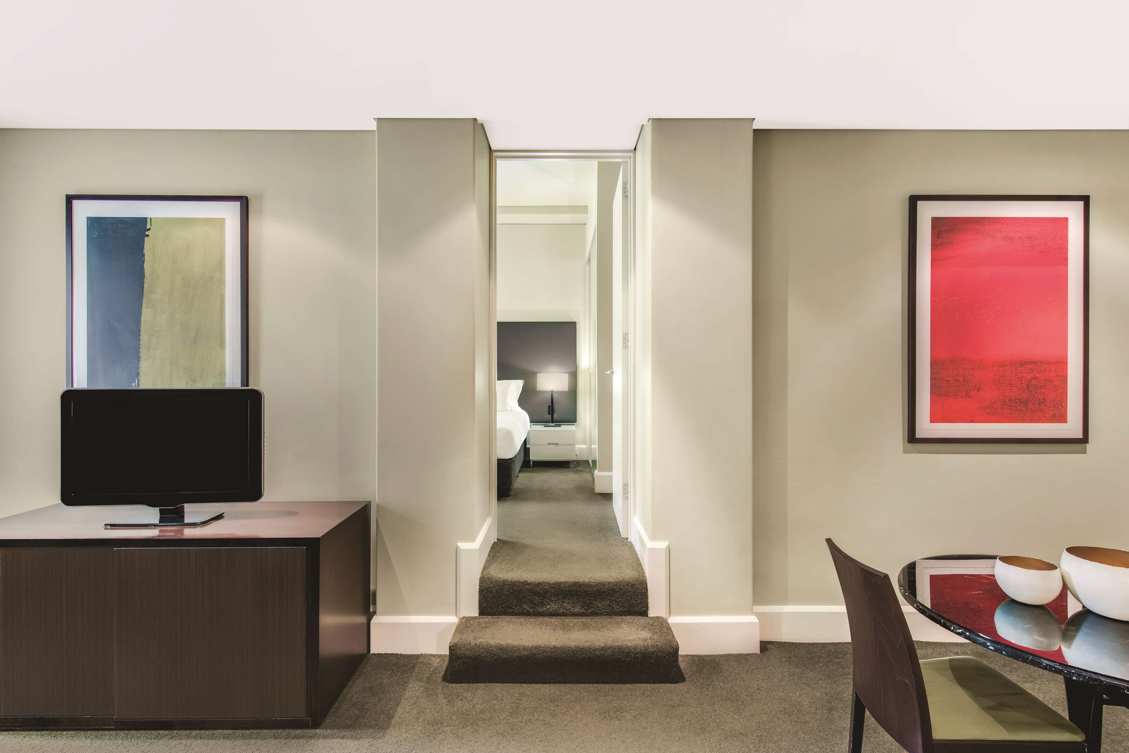 Ein Hotelzimmer mit einem Flachbildfernseher auf einem Holztisch, einem Esstisch mit Stühlen und einer Treppe, die in ein weiteres Zimmer führt.