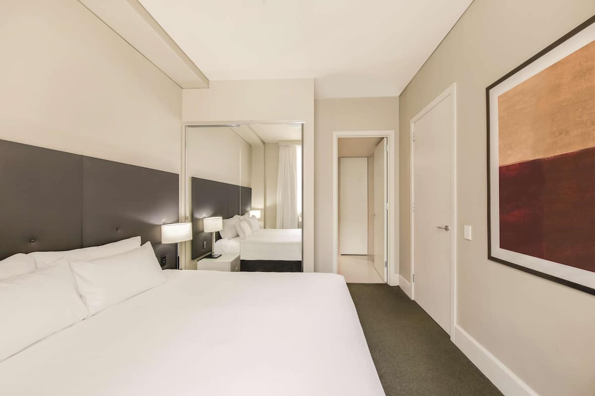 A hotel room with a large bed, a bedside table with a lamp, a mirror, and a door leading to another room.