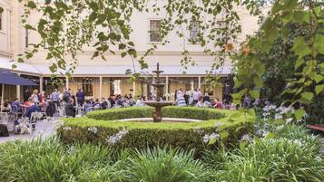 An outdoor café with a central fountain, surrounded by neatly trimmed hedges and lush greenery.