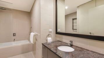 A modern bathroom with a bathtub, a sink with a granite countertop, and a large mirror.